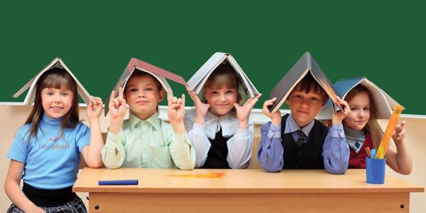 School children sitting at a desk and balancing books on their heads